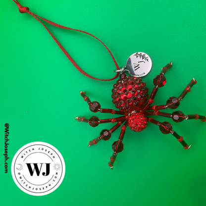 red spider holiday ornament on green background with the Witch Joseph logo