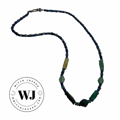 Beaded necklace with blue, green, and yellow beads, Roman glass and lapis lazuli on a white background, featuring the Witch Joseph logo