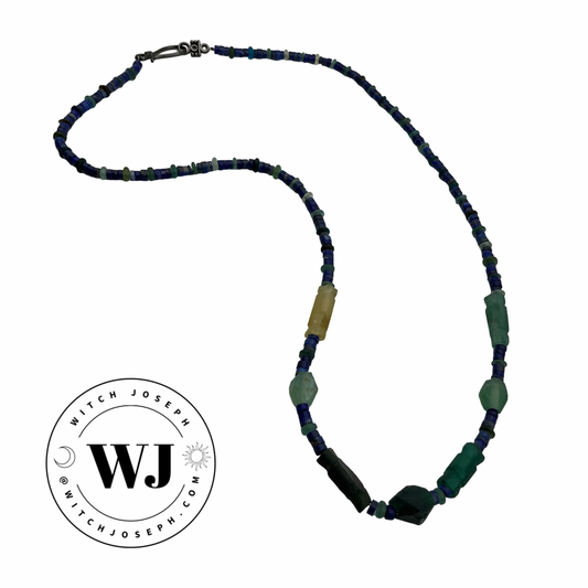 Beaded necklace with blue, green, and yellow beads, Roman glass and lapis lazuli on a white background, featuring the Witch Joseph logo