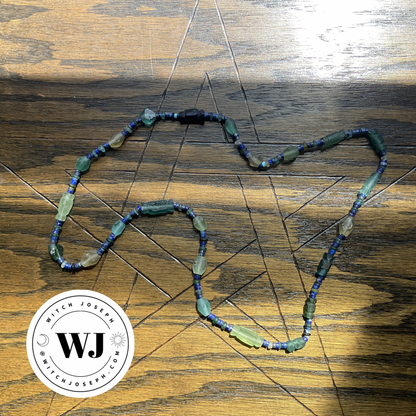 Ancient Roman glass beads in green, yellow and blue with lapis lazuli beaded necklace displayed on a wooden plane with a pentagram etched into it with the Witch Joseph logo