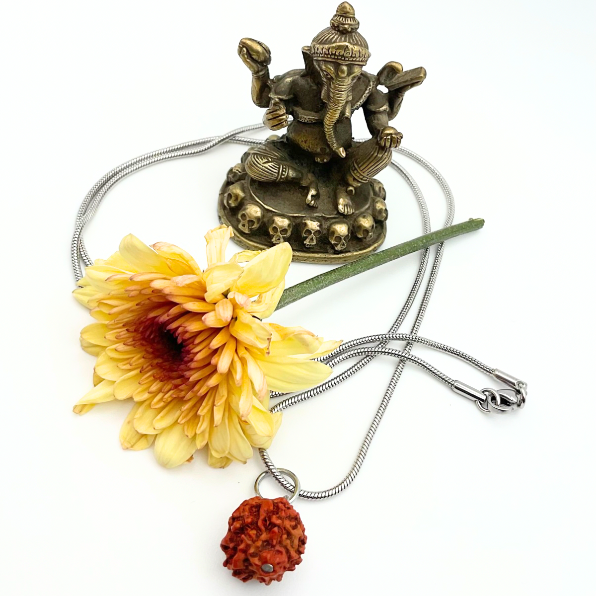 Necklace with Ganesha statue, yellow flower, and red rudraksha bead necklace on a white background