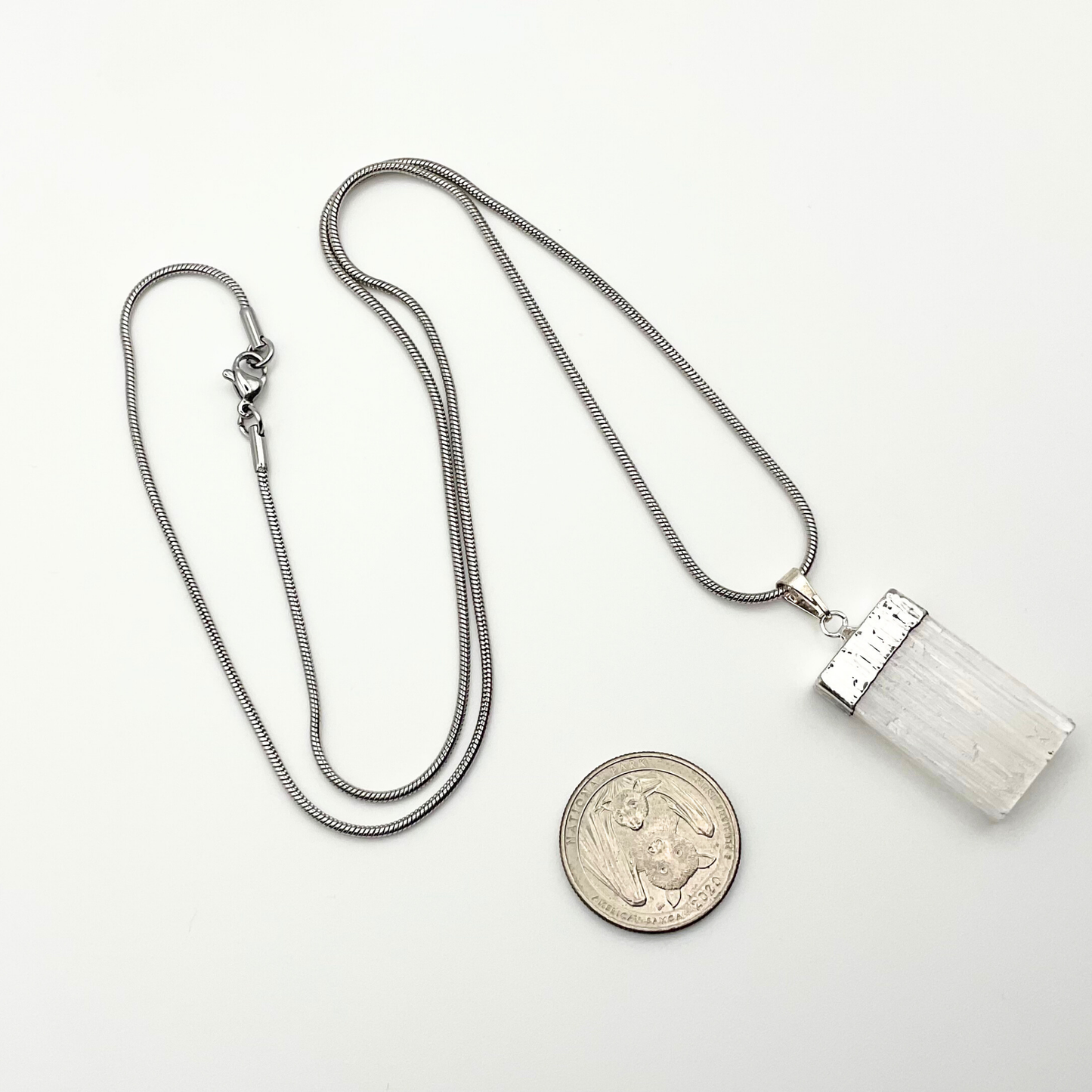 Silver necklace with a selenite pendant on a white background with white roses in a garden