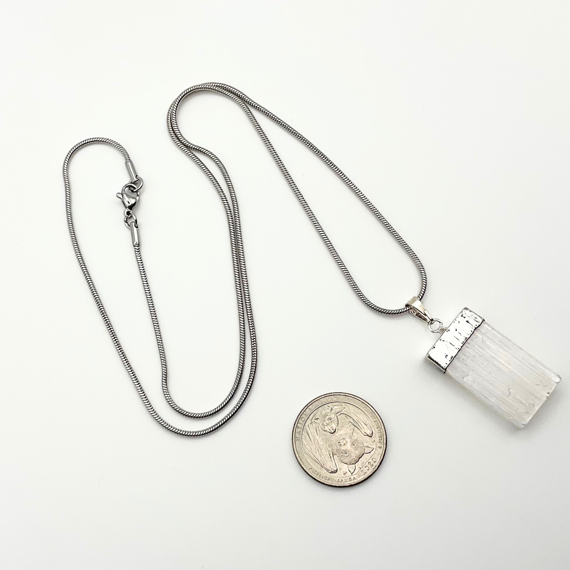 Silver necklace with a selenite pendant on a white background with white roses in a garden