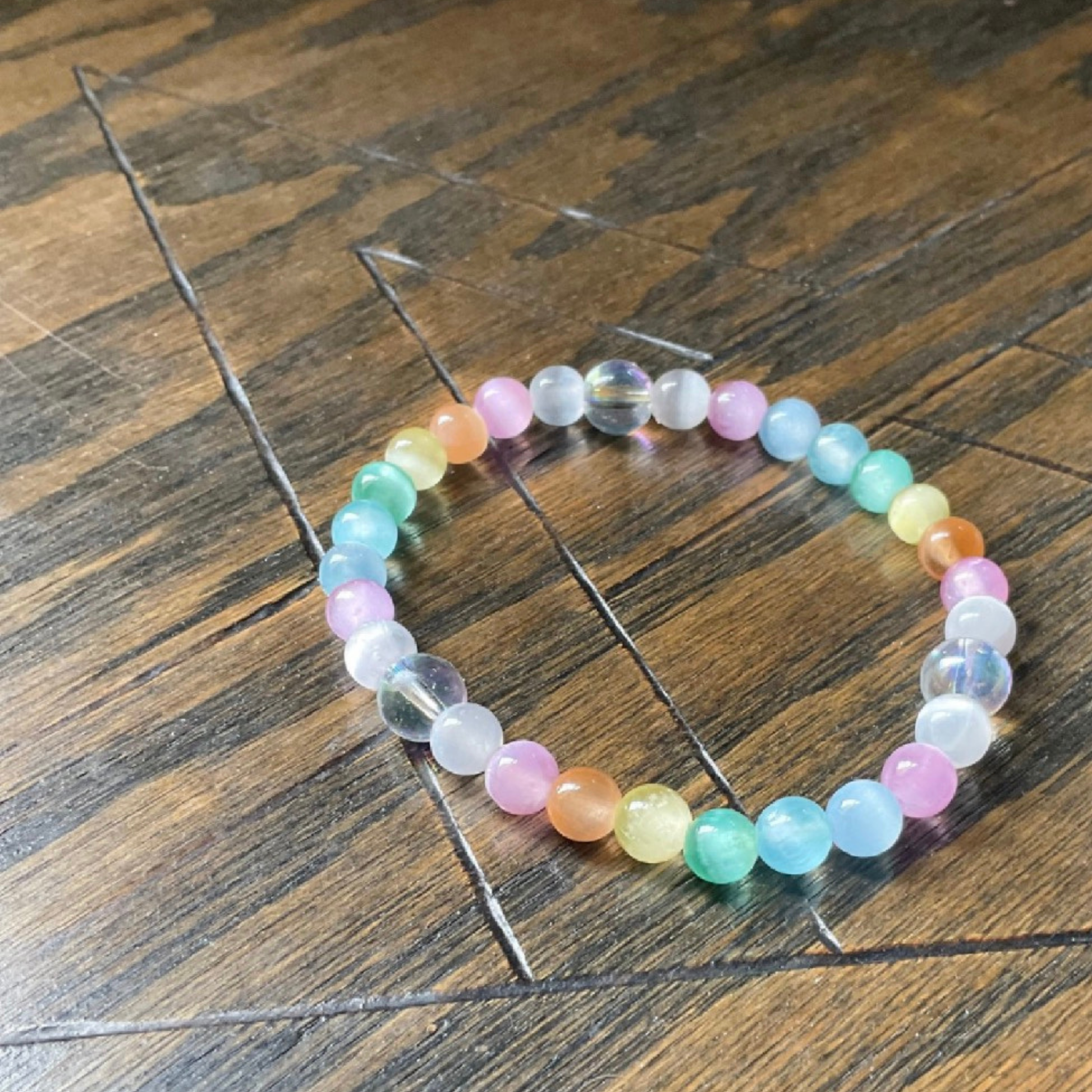 Colorful pastel selenite beaded bracelet displayed on a wooden surface with a pentagram etched into it