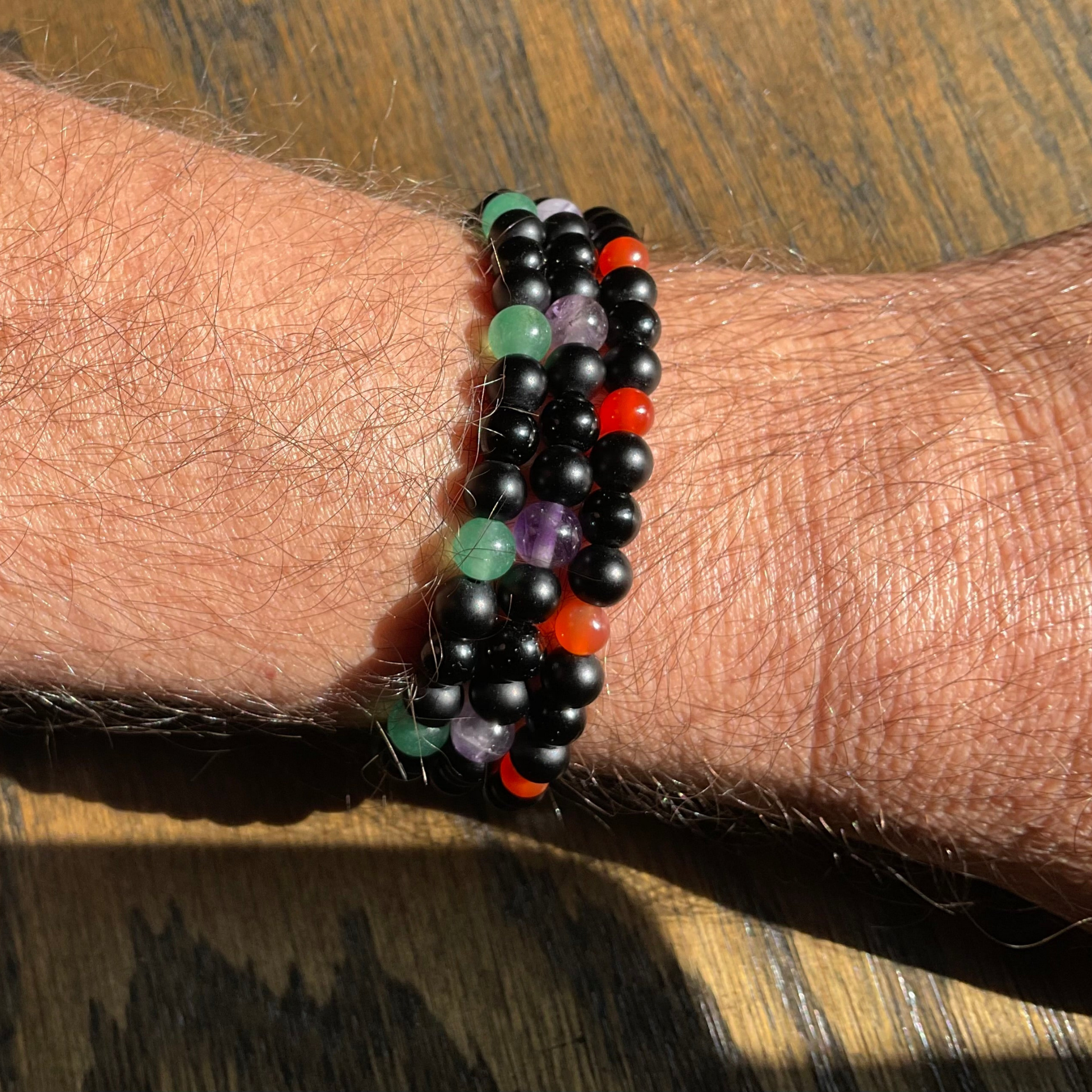 3 Multicolored amethyst carnelian and aventurine beaded bracelets with black beads being worn on a wrist over a wooden background