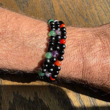 3 Multicolored amethyst carnelian and aventurine beaded bracelets with black beads being worn on a wrist over a wooden background