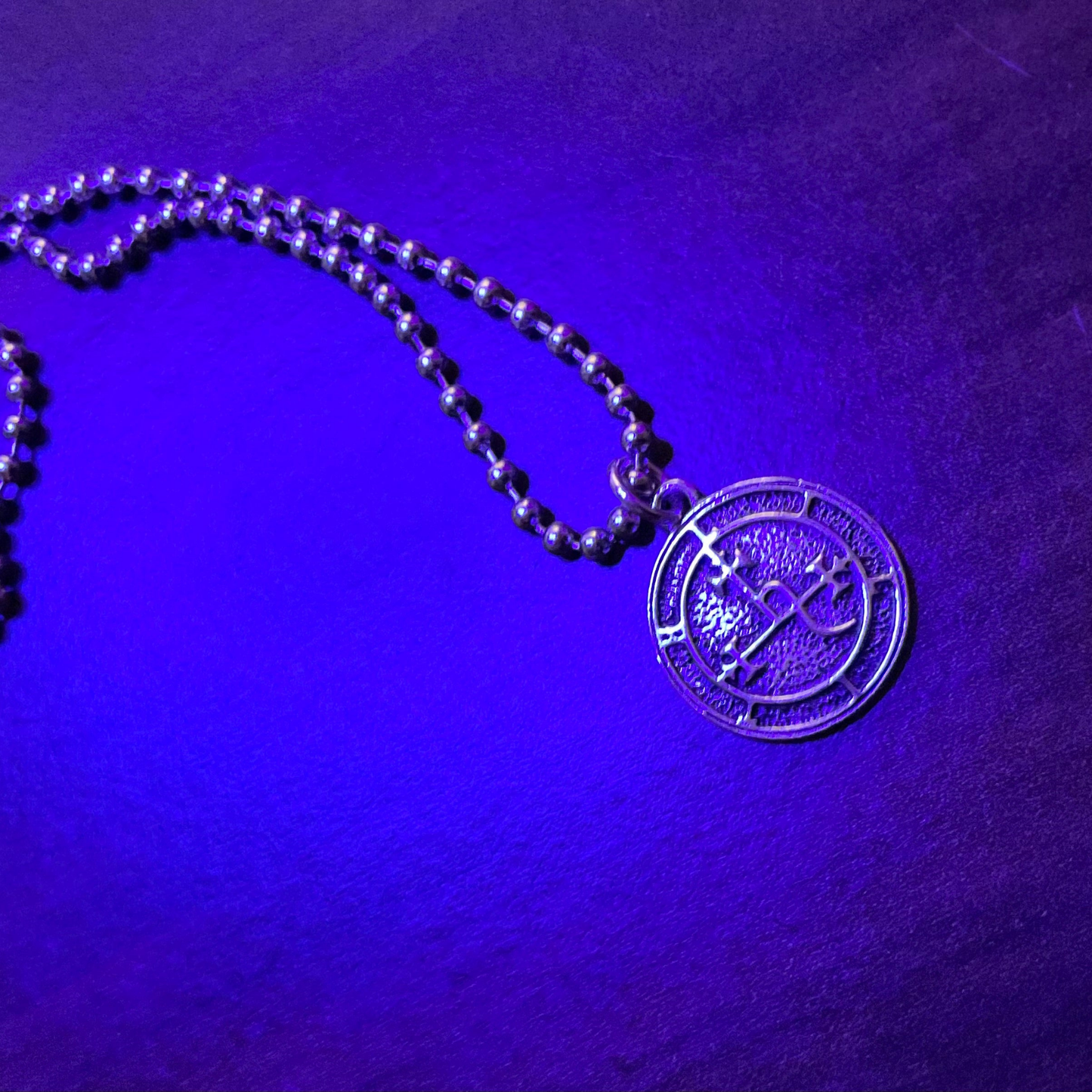 Lilith Sigil Charm Necklace with a round silver tone Lilith Sigil pendant on a purple textured background