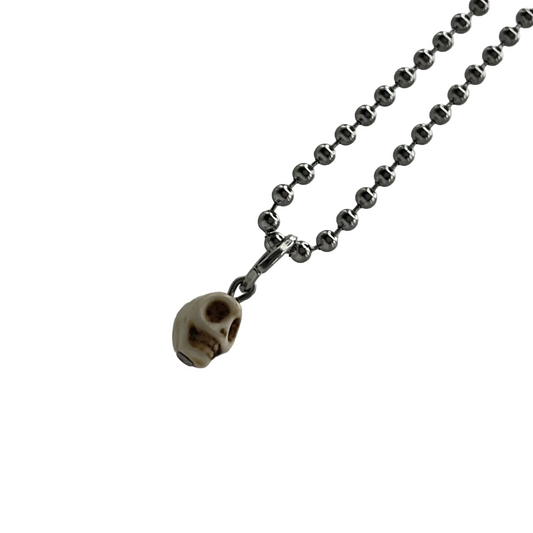 Small and delicate Skull pendant on a ball chain charm necklace against a white background