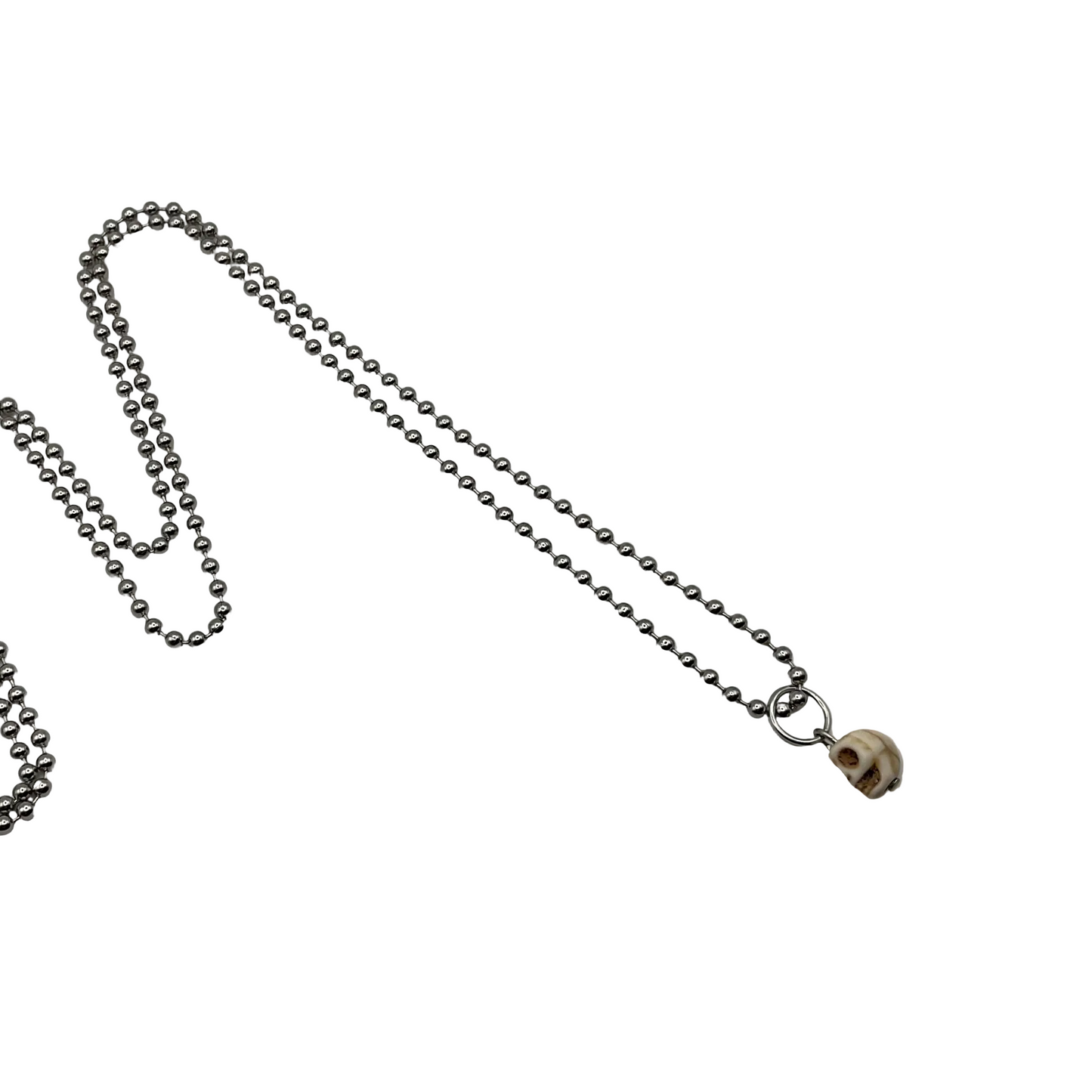 Silver tone chain ball chain necklace with a delicate skull pendant on a white background