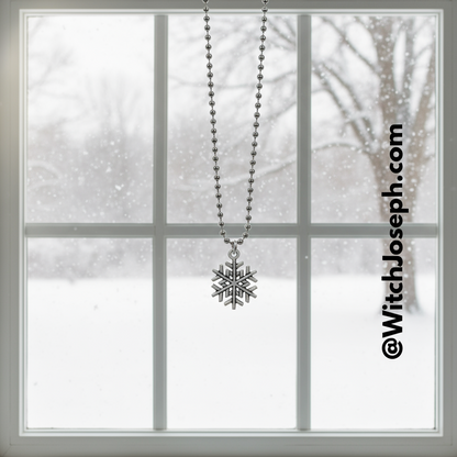 Snowflake charm necklace hanging in front of a window with a snowy scene