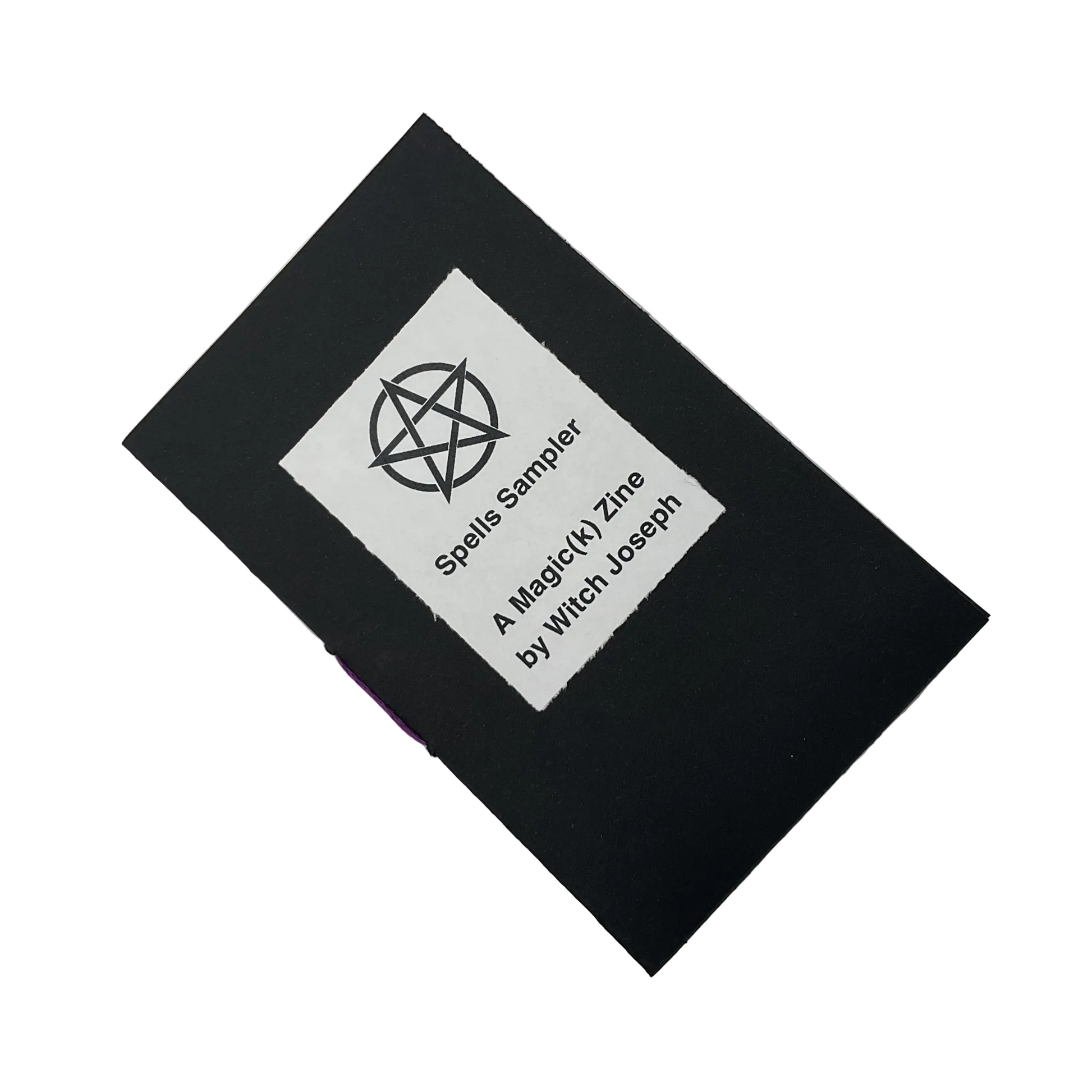 Black zine with a white label featuring text that says Spells Sampler…displayed on a white background