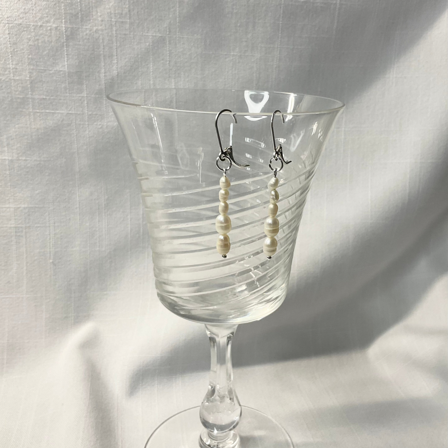 Sterling freshwater pearl dangle earrings displayed against white fabric on a crystal wine glass