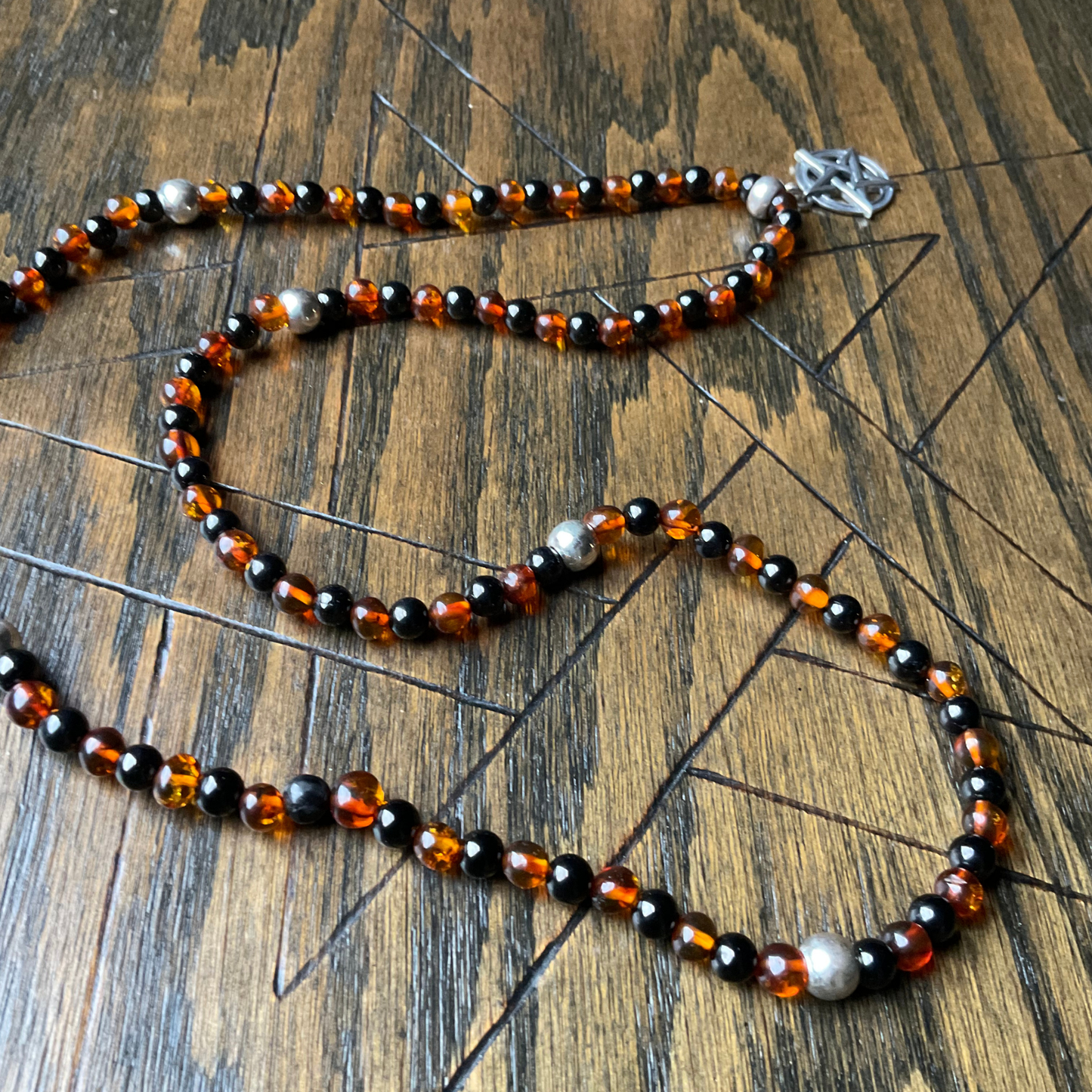 Amber and Jet Beaded necklace with sterling silver accent beads and a Sterling Silver Pentacle displayed on a wooden surface.