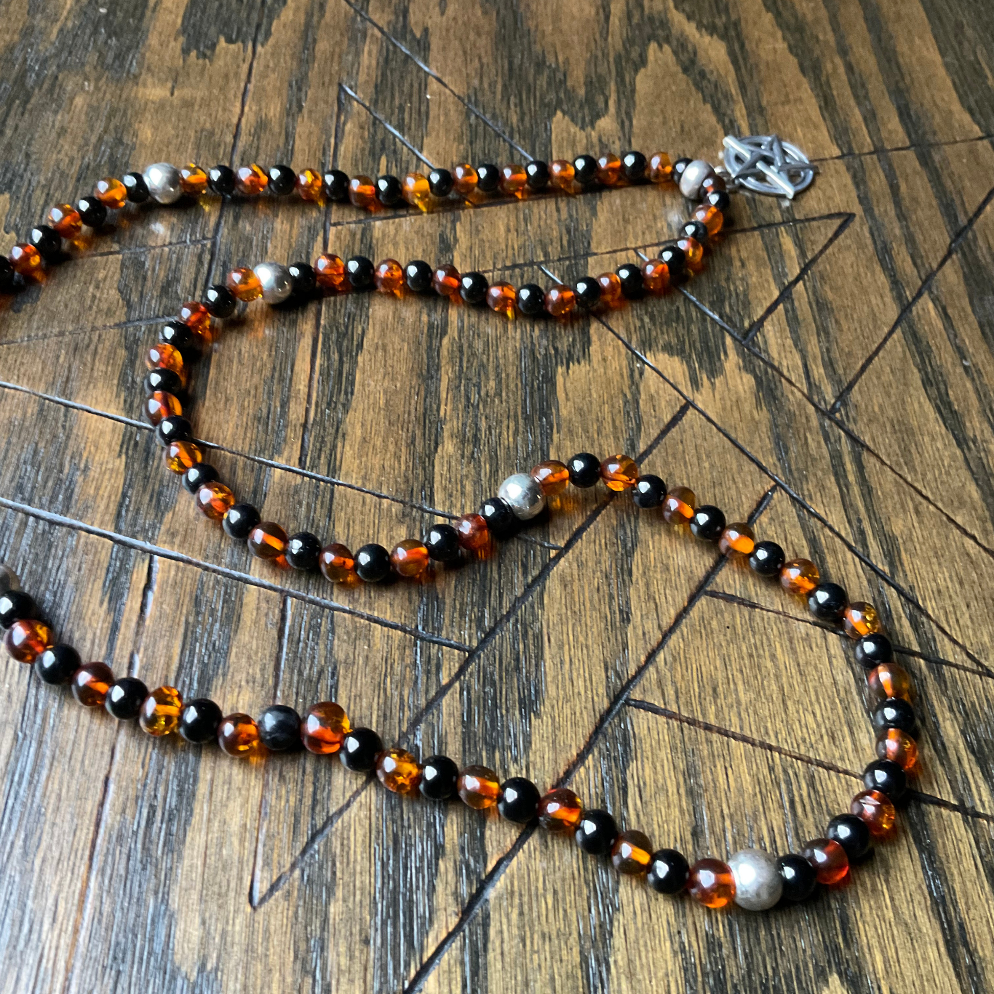 Amber and Jet Beaded necklace with sterling silver accent beads and a Sterling Silver Pentacle displayed on a wooden surface.