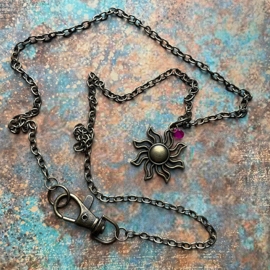 Bronze tone Necklace with sun-shaped pendant with small pink crystal displayed on a textured surface