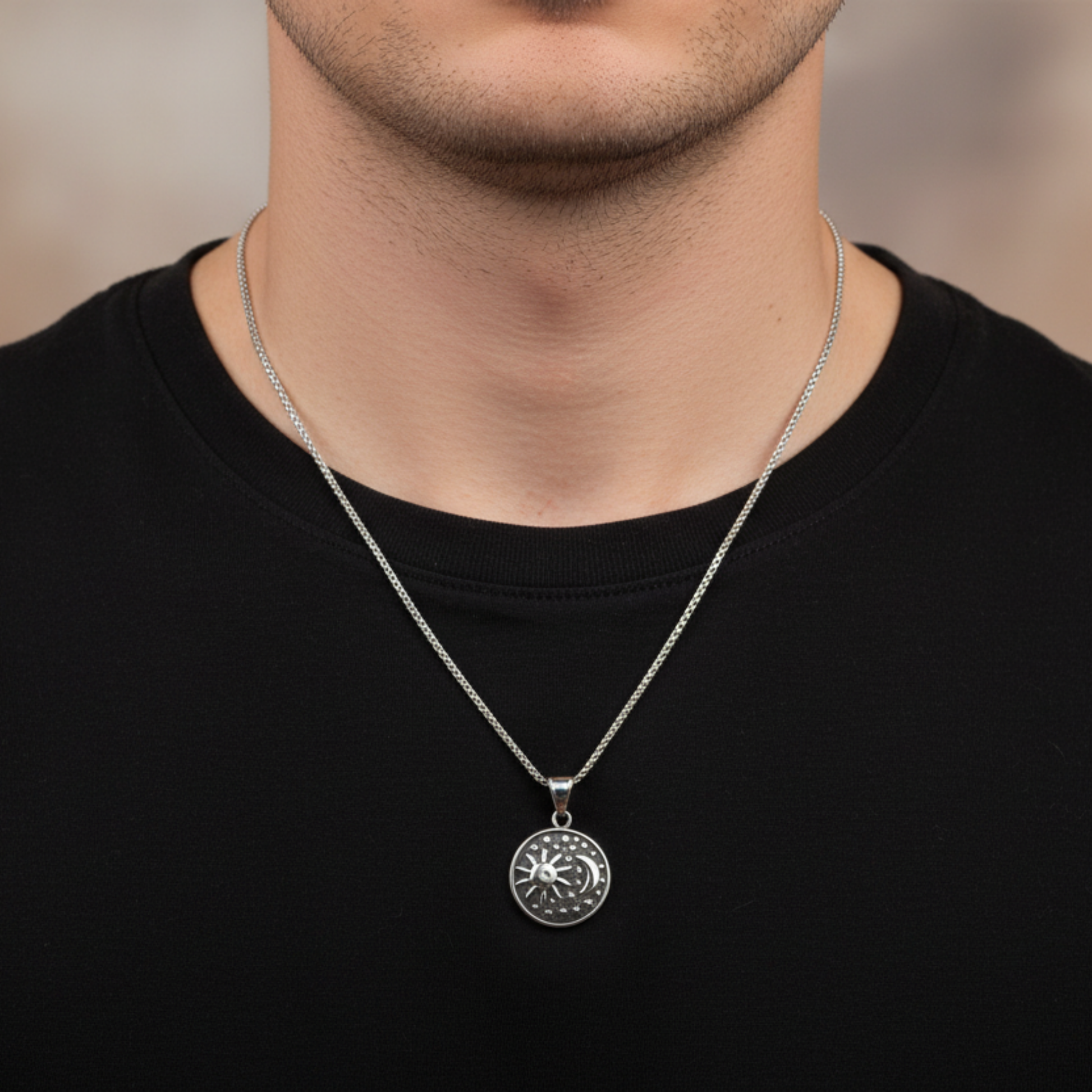 Man wearing a black shirt and wearing a silver tone necklace featuring a round pendant with Sun Moon and Stars
