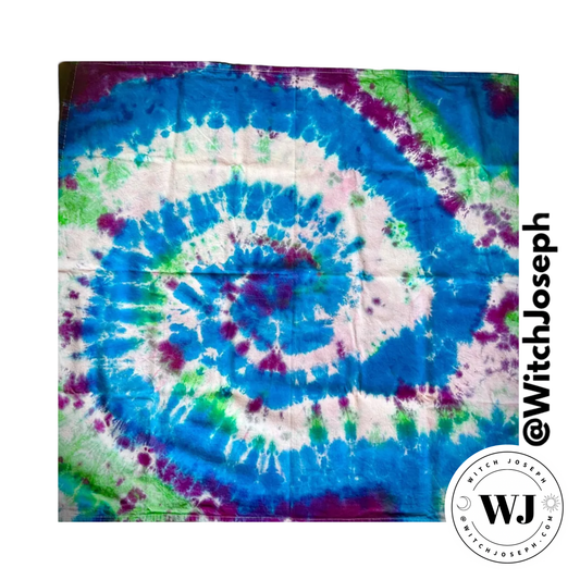 Tie-dye tarot cloth or altar cloth with spiral pattern in blue, green, purple, and white, branded with 'Witch Joseph'.