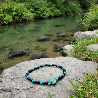 Black and turquoise tone stretch Bracelet with turtle bead laying on a rock by a stream with turtles in the background