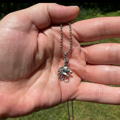 Hand holding a silver tone Unicorn bust charm necklace against a natural background