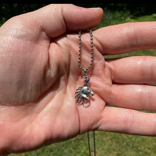 Hand holding a silver tone Unicorn bust charm necklace against a natural background