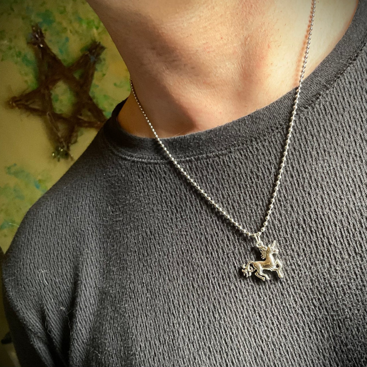 Person wearing a silver tone necklace with a unicorn pendant against a textured wall.