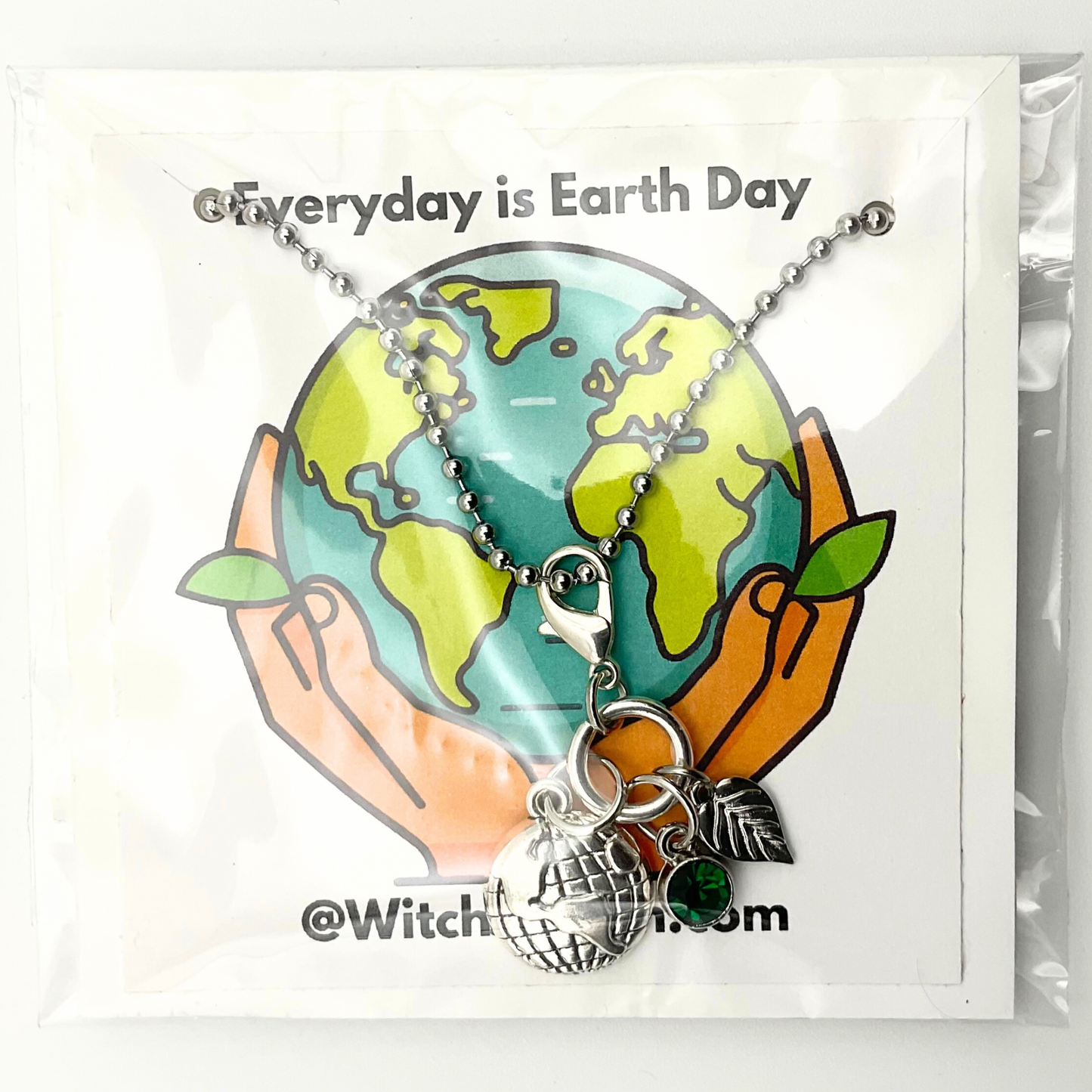 Earth Day Charm Necklace with a globe charm, silver tone leaf and a green crystal on a card that says 'Everyday is Earth Day' with a hand holding the Earth