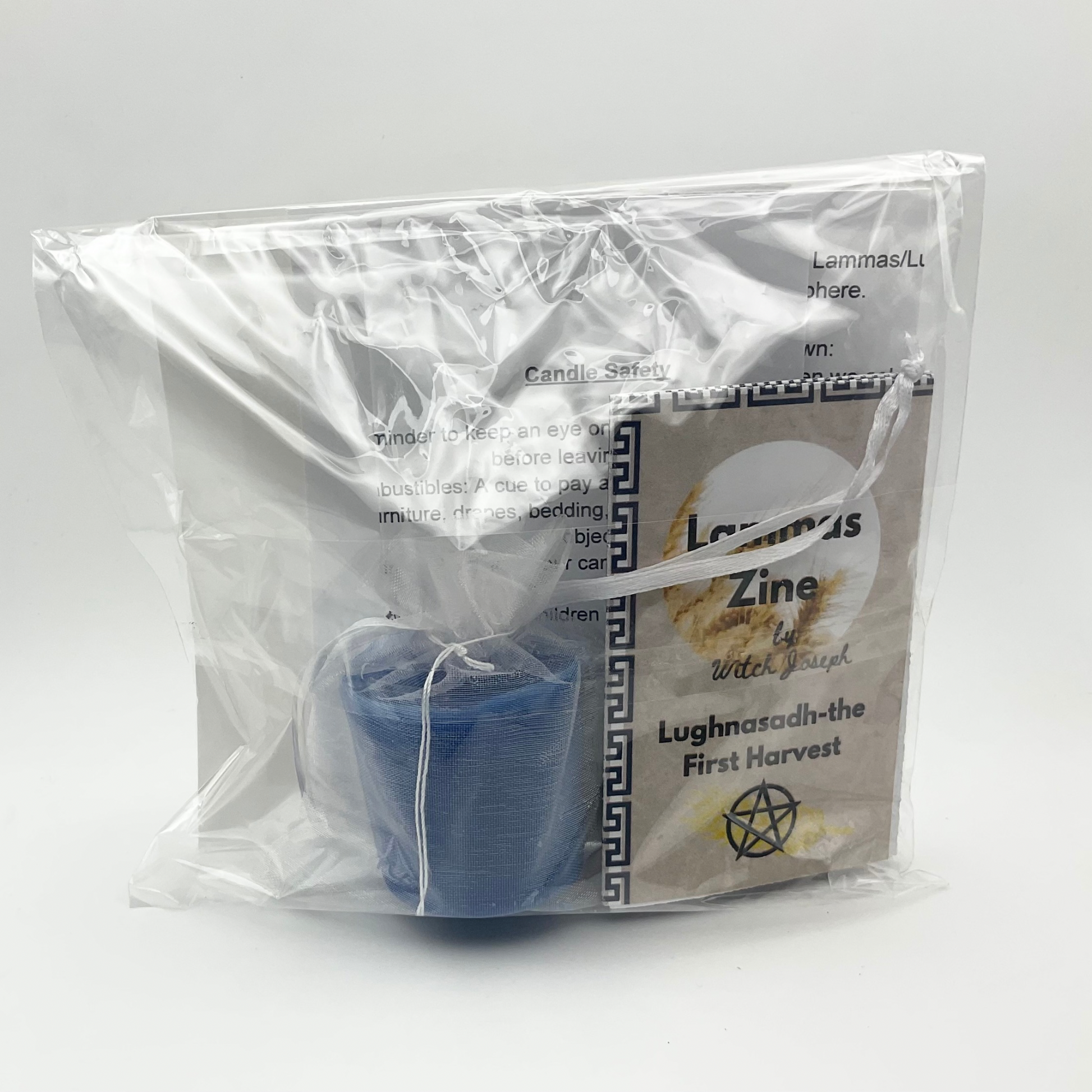 Product packaging with a Lammas blue candle and a Lammas zine inside a clear plastic packaging on a white back ground