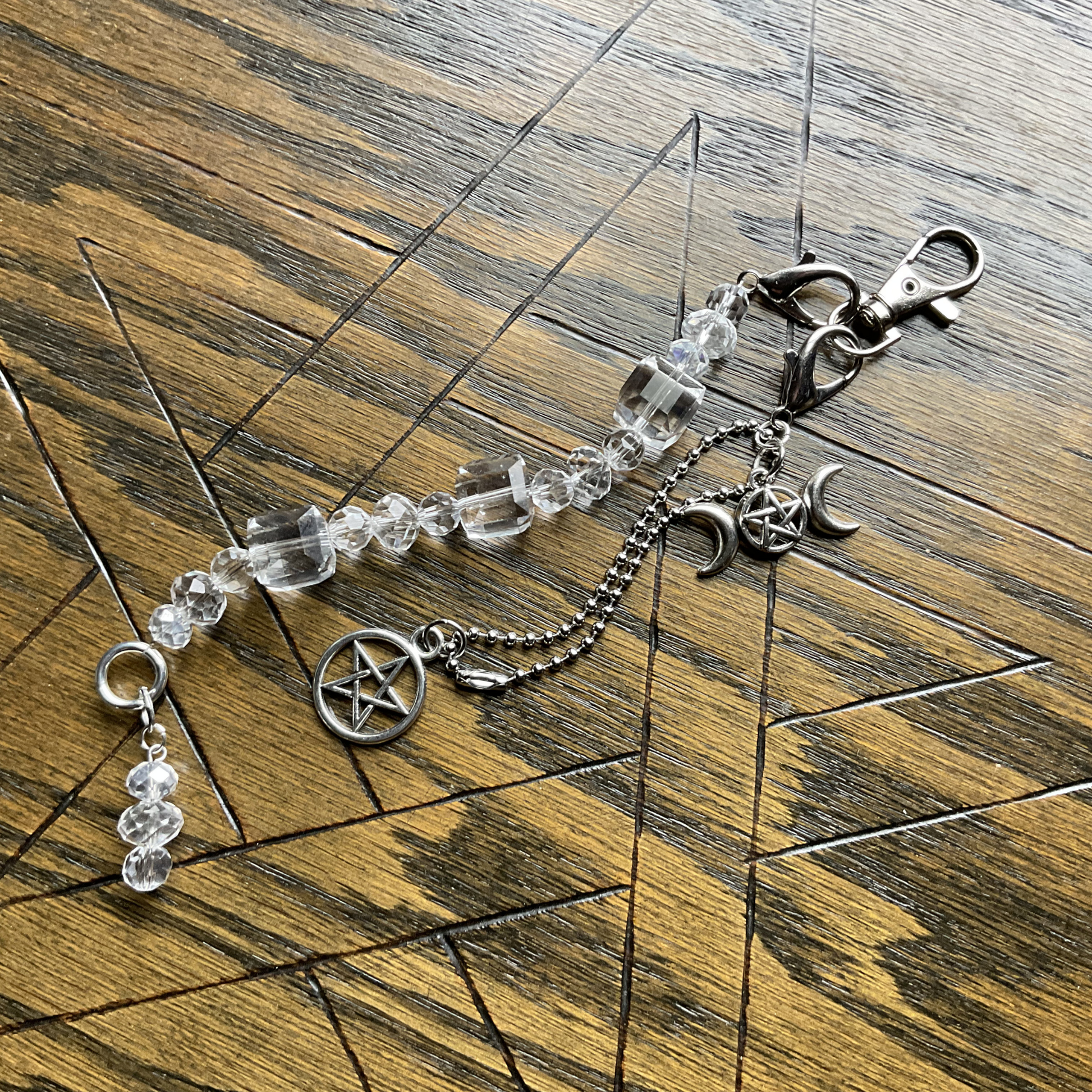 Purse Bag Charm with clear beads and silver tone pentacle and tripple Goddess charms displayed on a wooden surface which is etched with a Pentagram