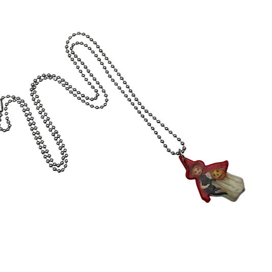 Necklace with a small pendant featuring a vintage style trick or treater character in a red hat holding a black cat and a jack o lantern pail on a light white background