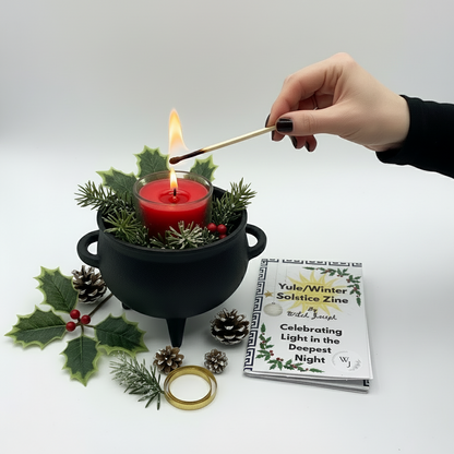 Yule Candle Kit being used…candle being lit in a cauldron with Yuletide items around it and the Witch Joseph Yule Zine close by…all against a white background.